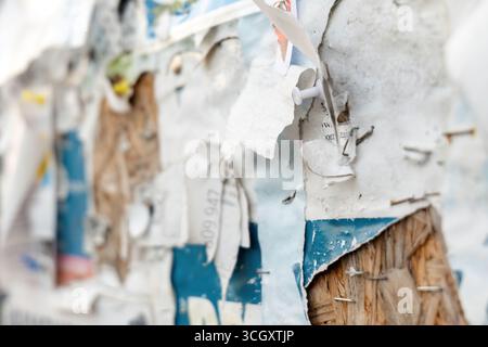 Torn paper scraps and staples on old community notice board, macro closeup of weathered announcements with peeling layers, push pin and nails on rough Stock Photo