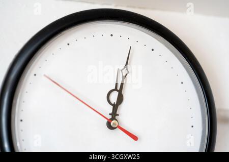 Minimal wall clock without numbers, analog dial with black hands red second hand on empty blank white face with dot markers closeup time management fl Stock Photo
