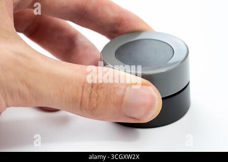 Finger adjusting a modern round grey black control knob isolated on white, closeup of a human hand turning a simple round dial, generic electronic dev Stock Photo