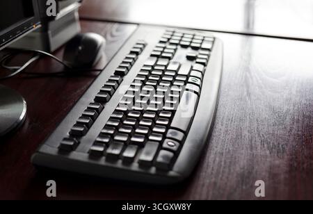 Black office keyboard on a wooden desk with a mouse and monitor in a quiet workspace shallow depth of field closeup of an ergonomic computer keyboard Stock Photo