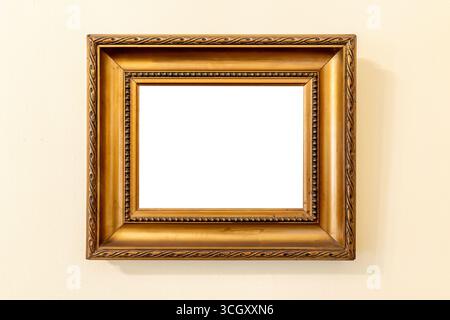 Small empty blank plain ornate square golden picture frame hanging on a beige wall, classic vintage border simple carved detail cut out inside border Stock Photo