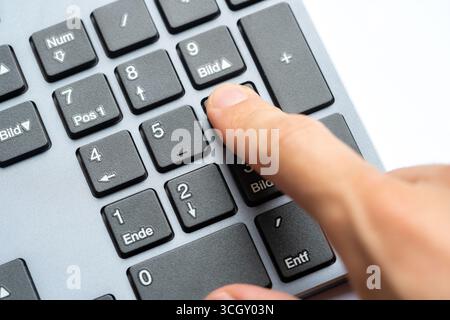 Closeup of an index finger pressing numeric keypad button on modern computer keyboard office data entry accounting manual spreadsheet calculations con Stock Photo