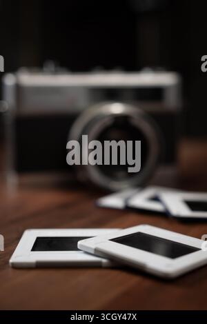 Close-up of photo slides lying on a wooden table with a vintage camera in the background, evoking nostalgia and memories of past travels Stock Photo