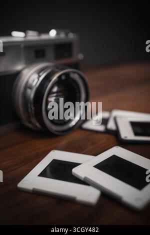 Vintage analog camera with lens and empty slides laying on wooden table against dark background representing memories and nostalgia Stock Photo