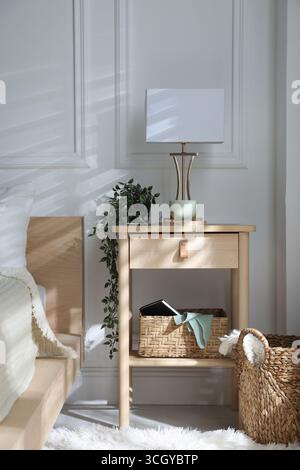 Bedside table with lamp and other decor near bed indoors Stock Photo