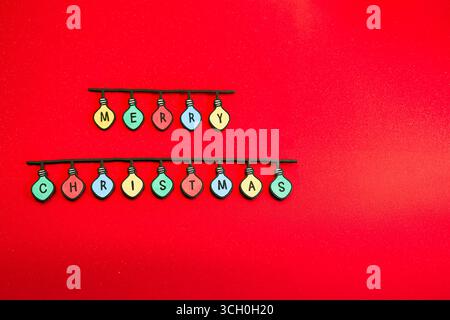 Festive Christmas decoration with light bulbs spelling out “Merry Christmas” on a bright red background. Concepts: Christmas greeting, joy, Christmas Stock Photo