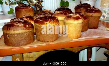 Ukrainian Easter cakes sit on a wooden table, showcasing their golden crusts and sweet toppings. Surrounded by greenery, they await festive gatherings Stock Photo