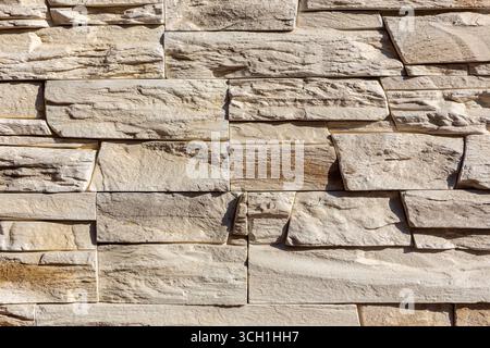 Light stone veneer cladding, decorative brick facing on a residential building facade in beige color. Stone and brick wall background. Stock Photo