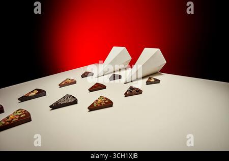 Artistic food styling featuring several chocolate bar pieces arranged in diagonal rows on a white surface, paired with angled white prism forms under Stock Photo