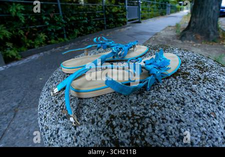 Broken blue women's sandals left behind on a round stone post next to an empty sidewalk, shallow depth of field. Stock Photo