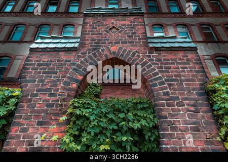Low angle view of ivy-covered brick arch on abandoned historic building with arched windows and weathered facade. Stock Photo
