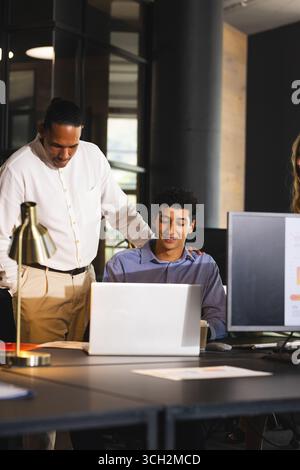 Collaborating on laptop, business diverse professionals discussing project details in modern office Stock Photo