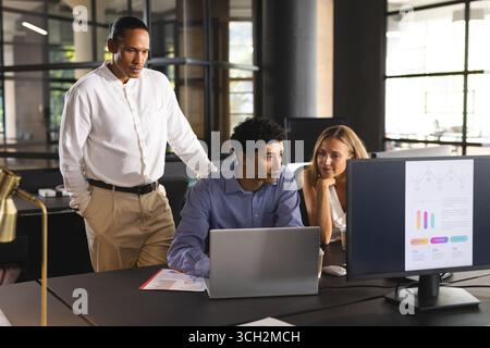 Diverse team collaborating on project, using laptops and discussing data in modern office Stock Photo