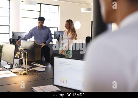 In office, diverse colleagues analyzing data on computer screens, discussing project details Stock Photo