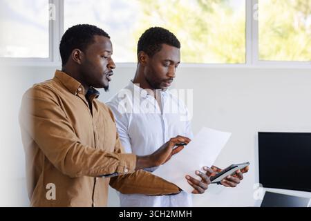 Two men discussing project details while reviewing documents in modern office Stock Photo