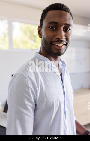 Confident man smiling in office, wearing casual shirt, standing near desk Stock Photo