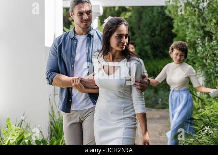 Bride and groom walking through garden, celebrating small casual wedding day with friends Stock Photo