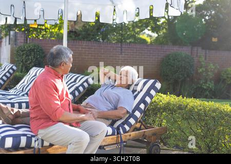 Senior couple relaxing on striped lounge chairs in sunny backyard garden Stock Photo