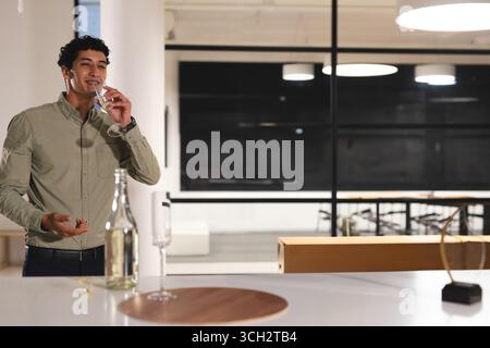 young man standing at counter in office bar sipping from glass with decanter nearby, copy space Stock Photo