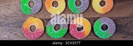 Colorful sugar-coated gummy rings arranged neatly on a rustic wooden background. Chewy, fruity candies with vibrant colors, ideal for desserts, sweet Stock Photo