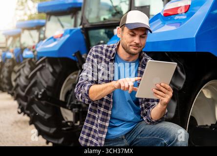 Man farm worker using digital tablet standing neat tractor outdoors Stock Photo