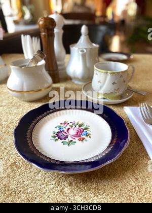 Elegant table setting with floral plate and tea set on luxurious golden fabric background. Mobile photo Stock Photo