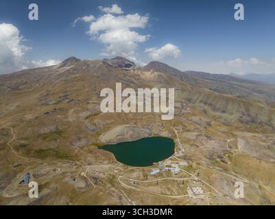 Aerial view of the emerald lake nestled beneath the stark, rocky peaks of Aragats Mountain under a vast sky, Lake Kari, Aragatsotn Province, Armenia. Stock Photo