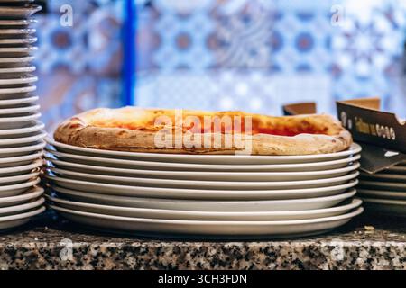 Fresh pizza resting on stacked white plates at restaurant counter Stock Photo