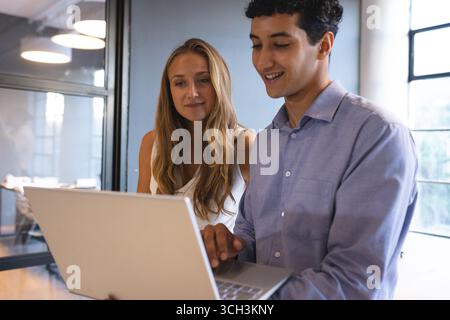 Diverse colleagues collaborating on laptop in modern office, discussing project details Stock Photo