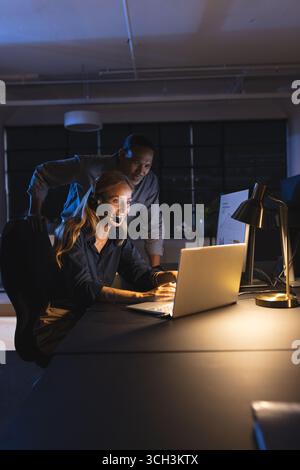 Business diverse professionals collaborating on laptop in modern office during night shift Stock Photo