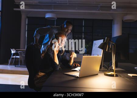 Business diverse professionals collaborating on laptop and phone in modern office at night Stock Photo