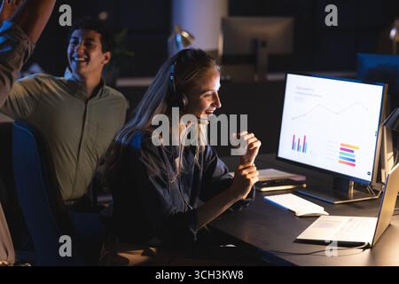 Businesswoman wearing headset analyzing data on computer at night office Stock Photo