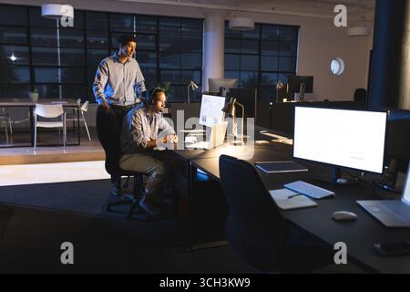 Business diverse professionals collaborating on project in modern office during night Stock Photo