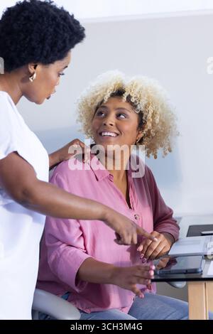 Two women collaborating at desk, using tablet and smiling in office Stock Photo