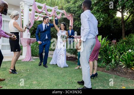 Bride and groom joyfully dancing outdoors with guests celebrating around them Stock Photo