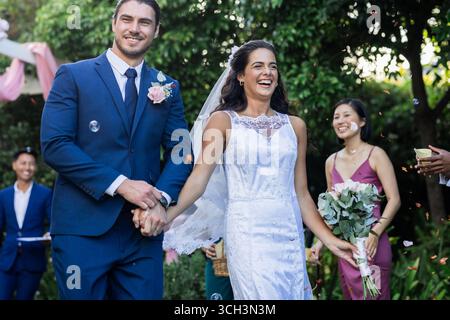 Bride and groom walking joyfully down aisle, surrounded by smiling guests Stock Photo
