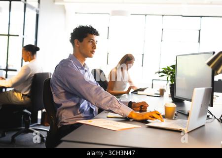 Focused businessman working on computer in modern office with colleagues nearby Stock Photo