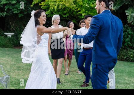 Bride and groom dancing joyfully on lawn with friends celebrating around them Stock Photo