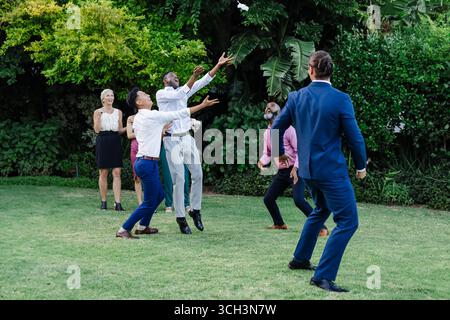 Catching bouquet joyfully, guests celebrating wedding in garden setting together Stock Photo