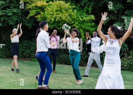 Guests celebrating joyfully outdoors, throwing bouquet at wedding reception Stock Photo