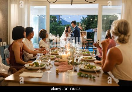 Bride and groom dancing joyfully while guests enjoy dinner at elegant reception Stock Photo