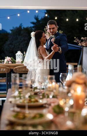 Bride and groom dancing joyfully under string lights at outdoor wedding reception Stock Photo