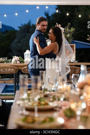 Bride and groom dancing joyfully at outdoor wedding reception under string lights Stock Photo