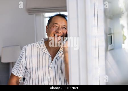 Smiling Senior Asian man talking on smartphone at home, enjoying conversation Stock Photo