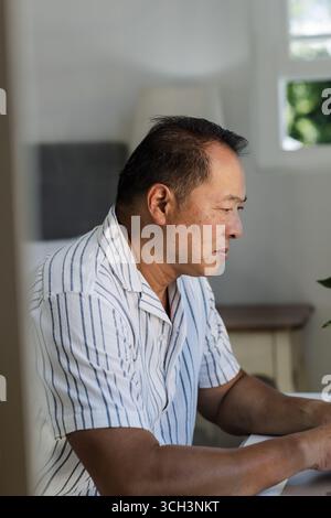 Senior man concentrating while using laptop at home, wearing striped shirt Stock Photo
