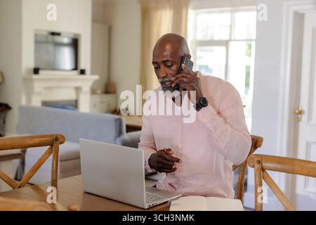 Senior man using smartphone and laptop at home, multitasking efficiently Stock Photo