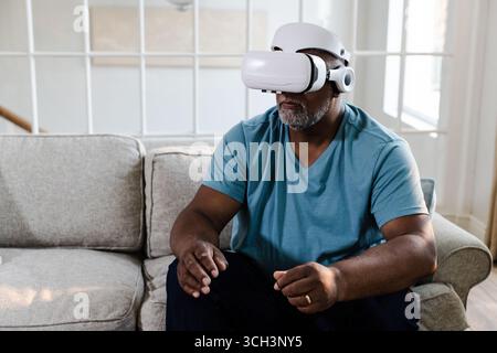 Senior African American man using VR headset sitting on sofa, experiencing virtual reality Stock Photo