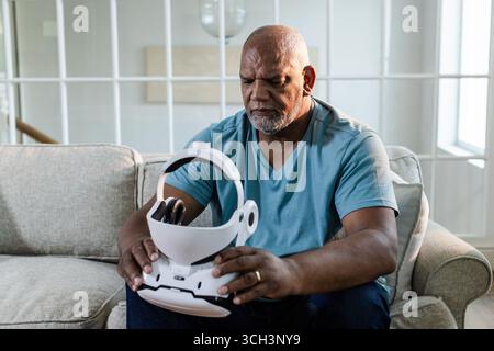 Senior man exploring virtual reality headset while sitting on living room sofa Stock Photo