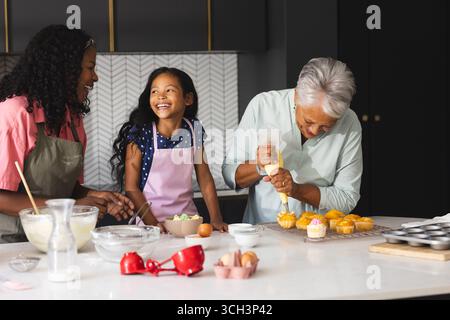 Three happy generations baking cupcakes in kitchen, sharing laughter and joy, at home Stock Photo
