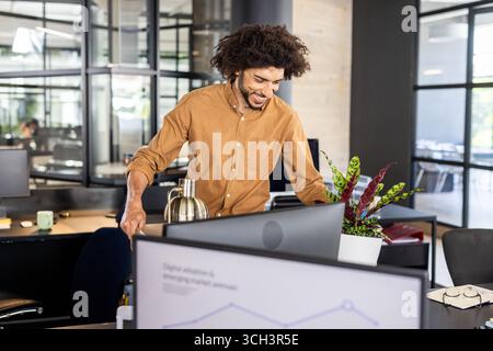 Asian man working on line graph at bright modern open-plan office, with coffee carafe and planter Stock Photo